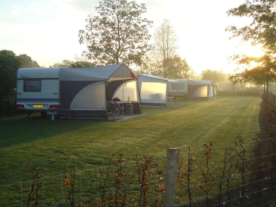 Kampeerplekken bij zonsopgang tussen bomen en hagen